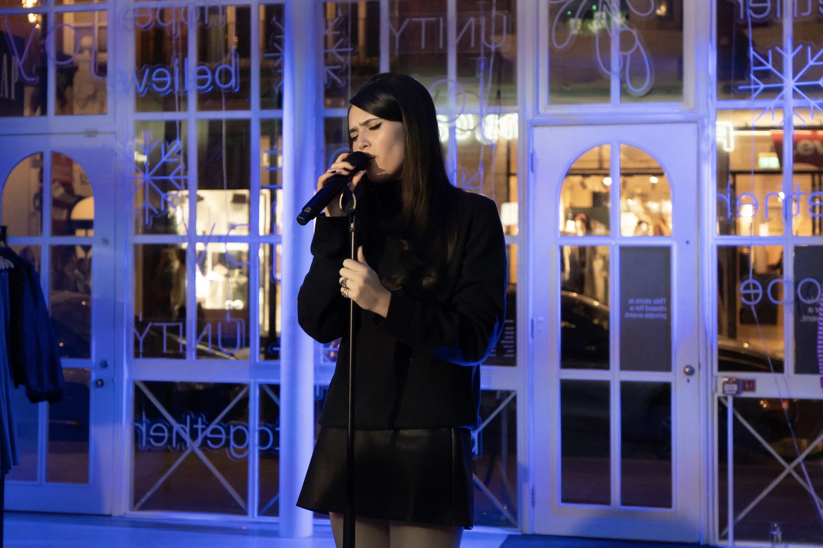Singer performing outside a storefront lit with blue neon signage