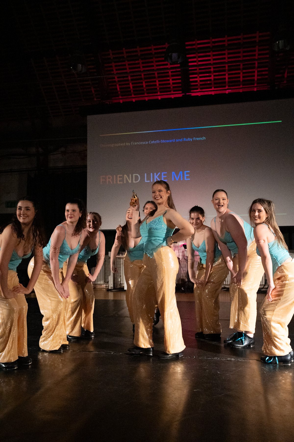 Dance group in turquoise and gold costumes celebrating with a trophy