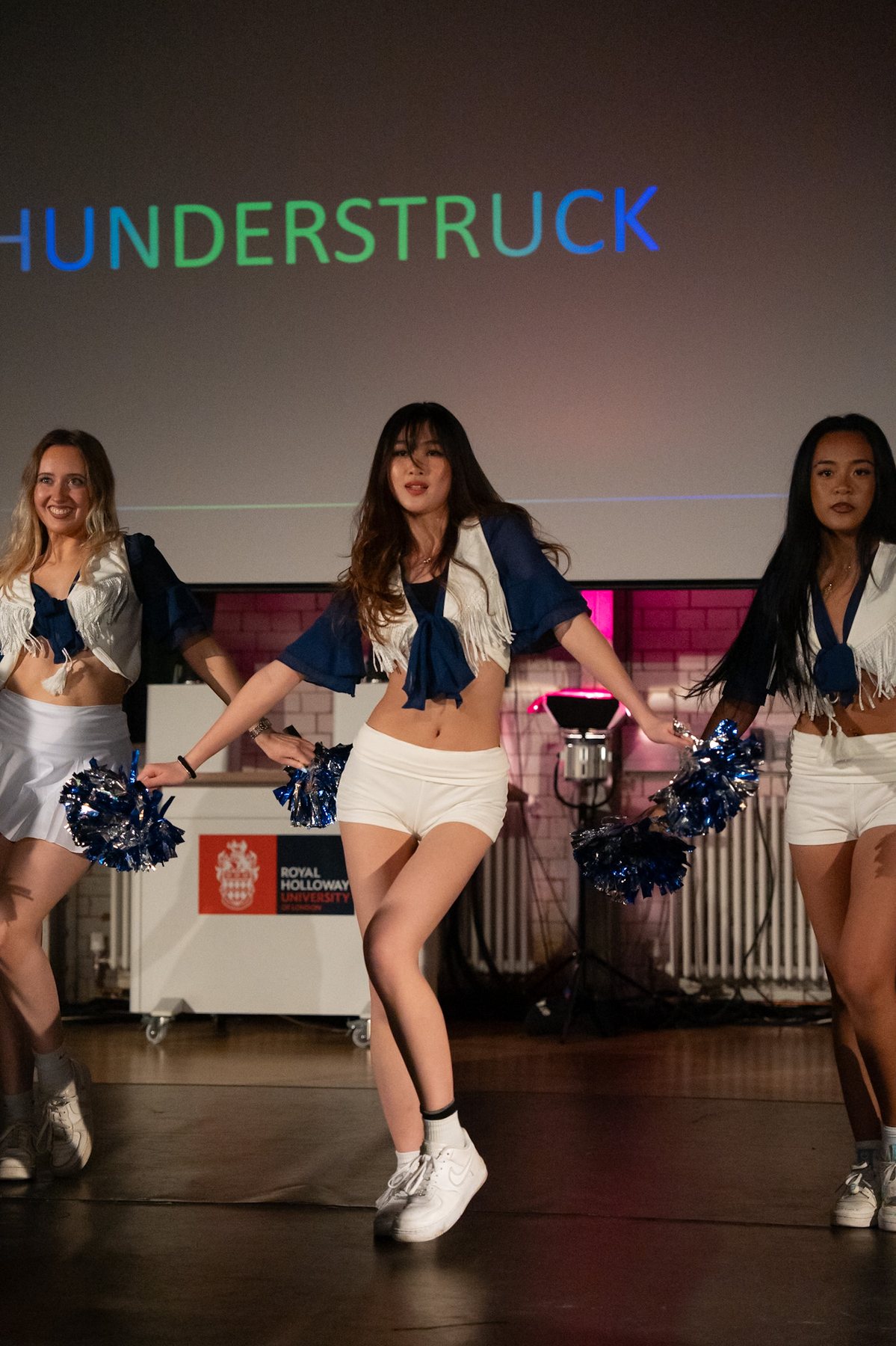 Dancers in navy and white cheer-style costumes under colourful stage light