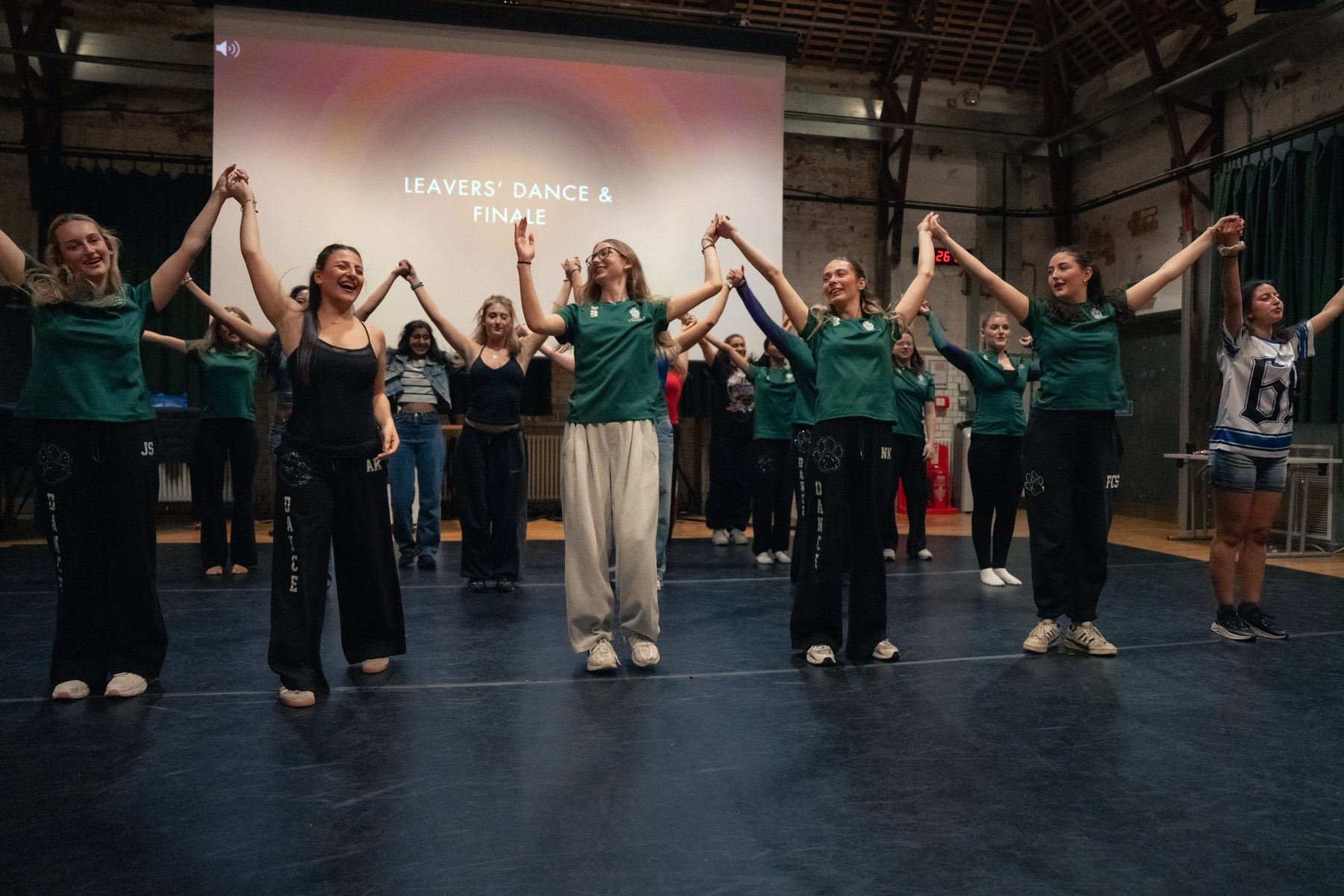 Dance ensemble in green shirts celebrating with hands raised